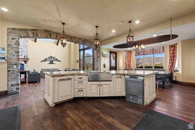 Kitchen featuring a wealth of natural light, dark wood-type flooring, light stone counters, a sink, and a notable chandelier | Image 23