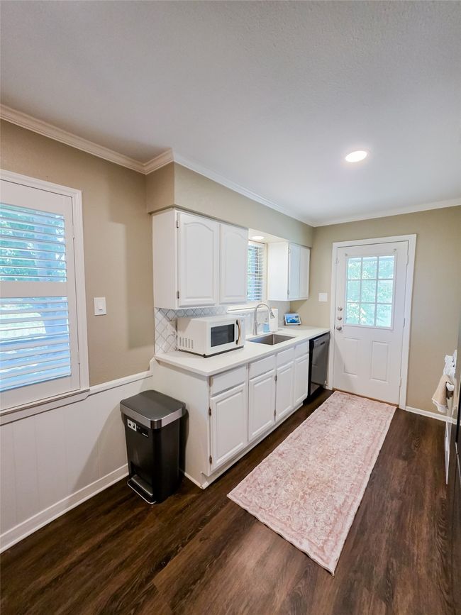 Kitchen featuring white microwave, black dishwasher, light countertops, a sink, and dark wood-style floors | Image 22