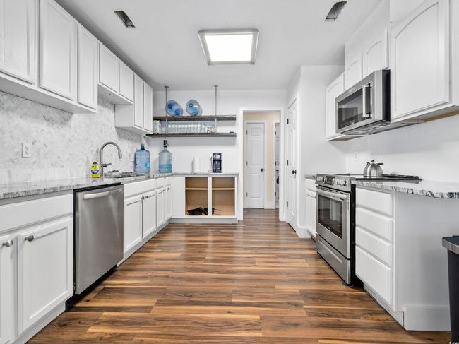 Kitchen featuring open shelves, dark wood-style floors, white cabinetry, light stone counters, and stainless steel appliances | Image 10