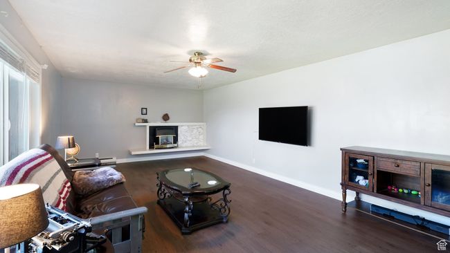 Living room with ceiling fan, wood finished floors, a glass covered fireplace, and baseboards | Image 10