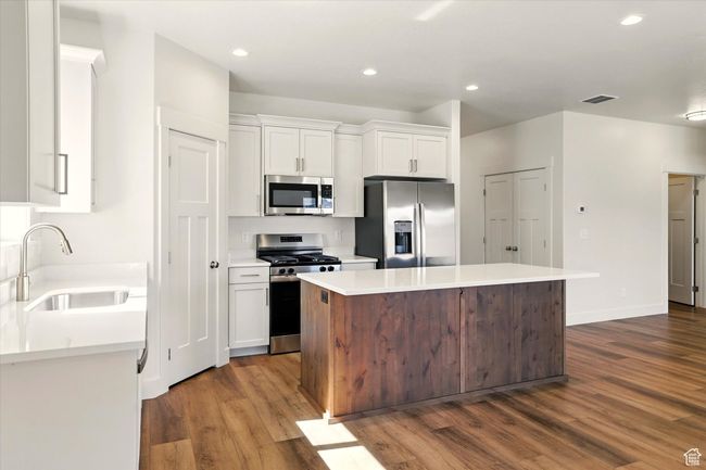 Kitchen featuring stainless steel appliances, a sink, dark wood-style floors, white cabinetry, and a center island | Image 12