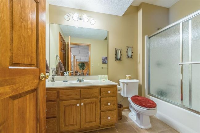 Bathroom featuring toilet, vanity, a textured ceiling, tile patterned floors, and enclosed tub / shower combo | Image 64