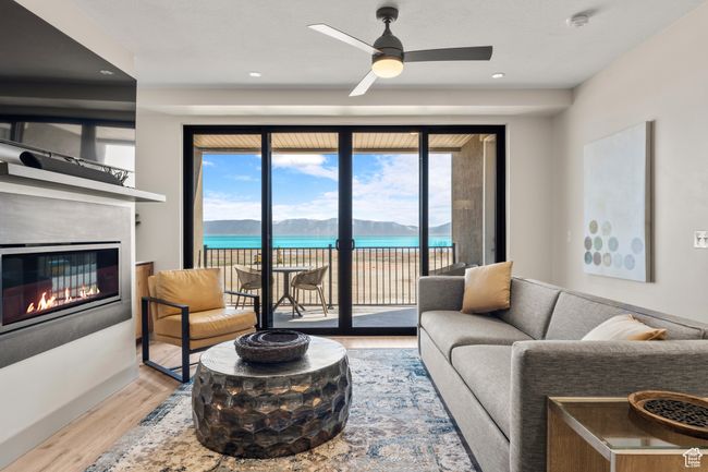 Living area with wood finished floors, a glass covered fireplace, a ceiling fan, recessed lighting, and a water view | Image 48
