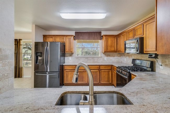 Kitchen with brown cabinetry, backsplash, stainless steel appliances, and a sink | Image 13