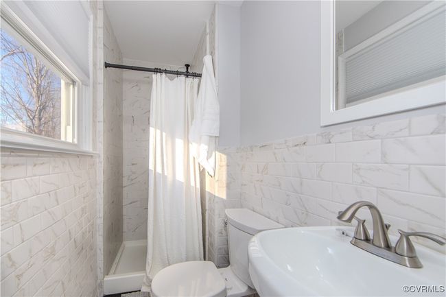Bathroom featuring a shower with curtain, toilet, sink, and tile walls | Image 23