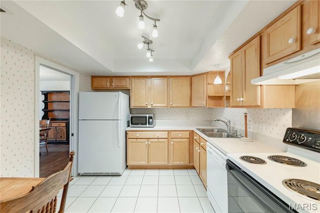 Kitchen featuring white appliances, a tray ceiling, light countertops, light brown cabinetry, and wallpapered walls | Image 23