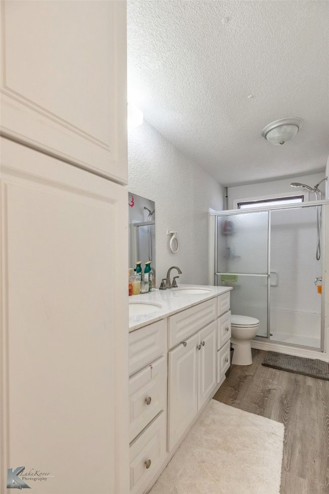 Bathroom with toilet, a stall shower, a sink, wood finished floors, and double vanity | Image 16