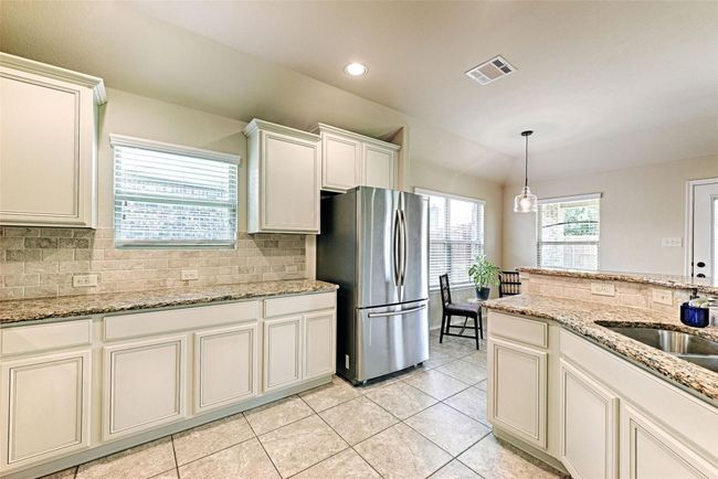 Kitchen featuring freestanding refrigerator, tasteful backsplash, light tile patterned floors, hanging light fixtures, and recessed lighting | Image 24