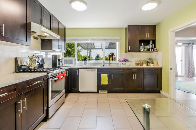 Kitchen with white appliances, under cabinet range hood, a sink, backsplash, and light countertops | Image 30