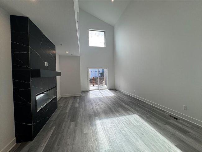 Unfurnished living room featuring wood finished floors, high vaulted ceiling, a fireplace, and a wealth of natural light | Image 8