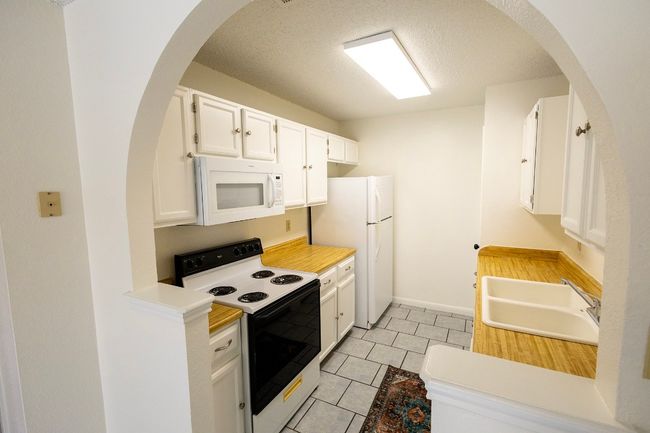 Kitchen with white appliances, a sink, light tile patterned floors, white cabinets, and light countertops | Image 27