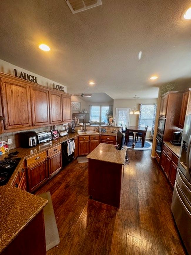 Kitchen with a peninsula, a textured ceiling, black appliances, and dark wood finished floors | Image 5