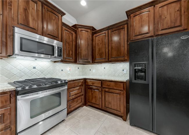 Kitchen featuring stainless steel appliances, light tile patterned floors, light stone counters, and decorative backsplash | Image 15