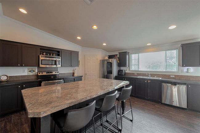 The kitchen features a large island at its center and has modern cabinetry, countertops, and various kitchen appliances, including an oven and microwave. | Image 14