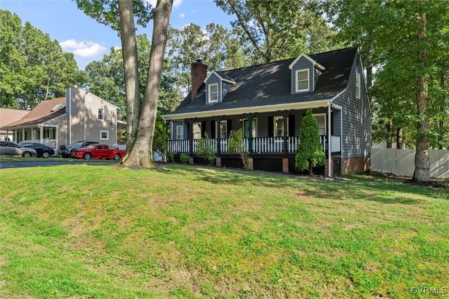 New england style home featuring a porch, a chimney, and view of wooded area | Image 5