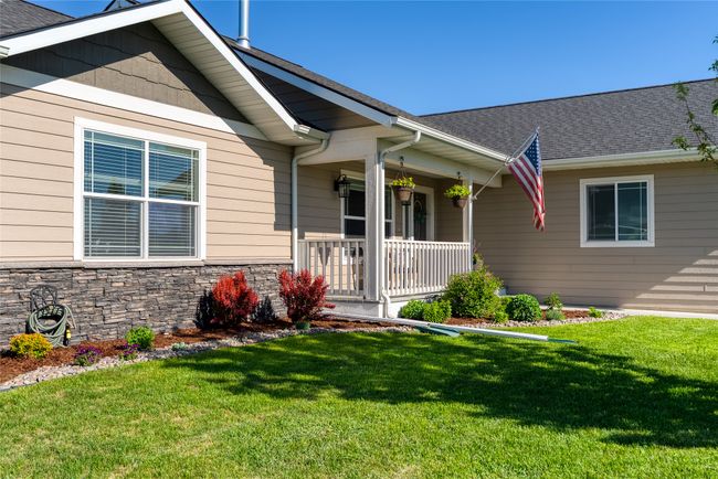 Doorway to property featuring a lawn, covered porch, stone siding, and roof with shingles | Image 5