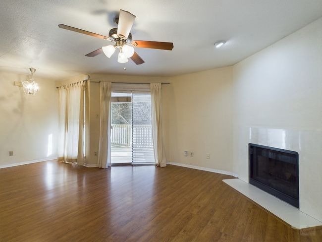 Unfurnished living room featuring a fireplace, wood finished floors, ceiling fan with notable chandelier, and baseboards | Image 8
