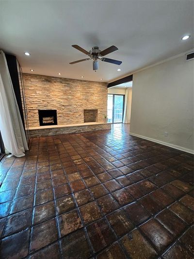 Unfurnished living room with a stone fireplace, ceiling fan, dark tile patterned flooring, and ornamental molding | Image 2