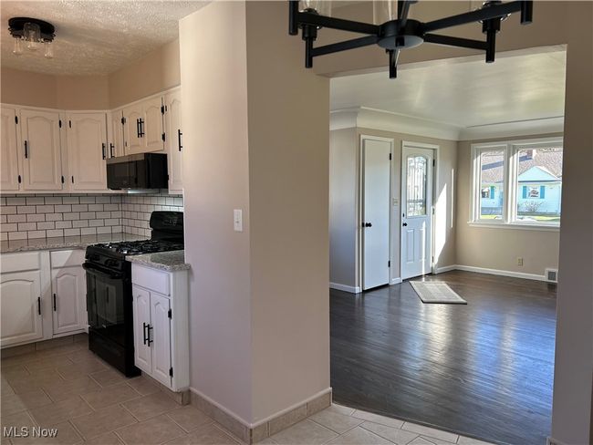 Kitchen featuring stainless steel microwave, white cabinets, decorative backsplash, granite countertops, and black range with gas cooktop | Image 12