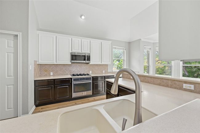 Kitchen with stainless steel appliances, vaulted ceiling, backsplash, a sink, and white cabinetry | Image 11