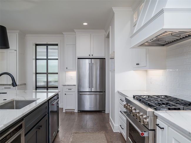 Kitchen featuring high quality appliances, custom exhaust hood, white cabinetry, tasteful backsplash, and recessed lighting | Image 11