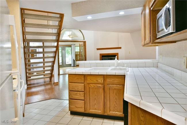 Kitchen with stainless steel microwave, tile counters, a ceiling fan, a fireplace, and brown cabinets | Image 12