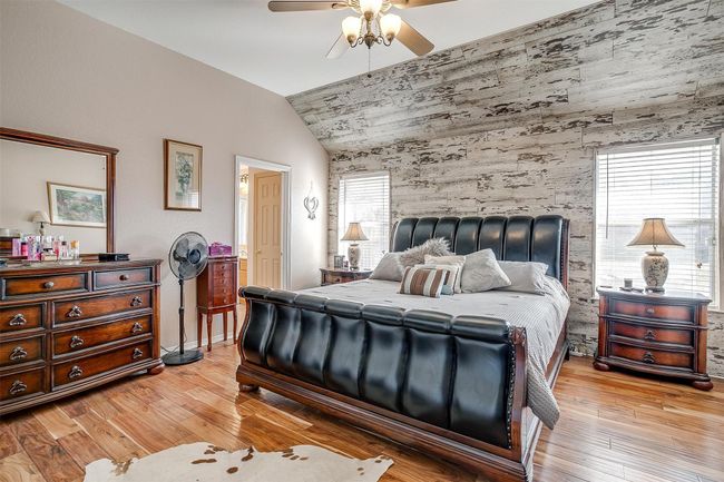 Bedroom featuring light wood finished floors, vaulted ceiling, an accent wall, ceiling fan, and wooden walls | Image 9