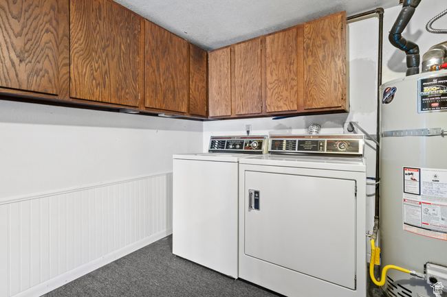 Washroom featuring secured water heater, separate washer and dryer, cabinet space, dark colored carpet, and a wainscoted wall | Image 33