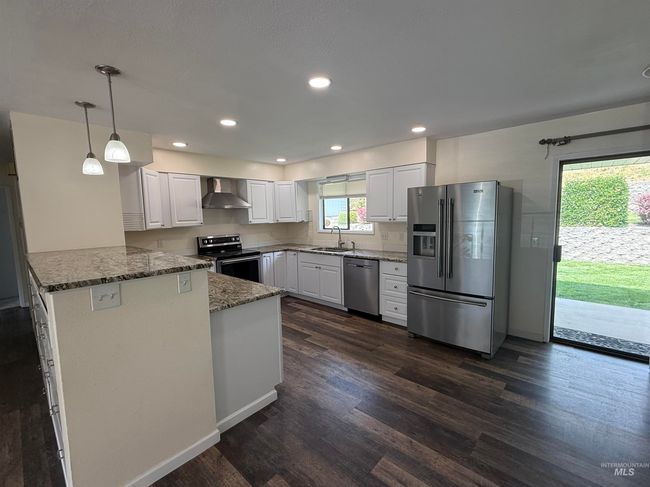 Kitchen featuring appliances with stainless steel finishes, wall chimney range hood, a peninsula, dark stone countertops, and dark wood-style flooring | Image 14