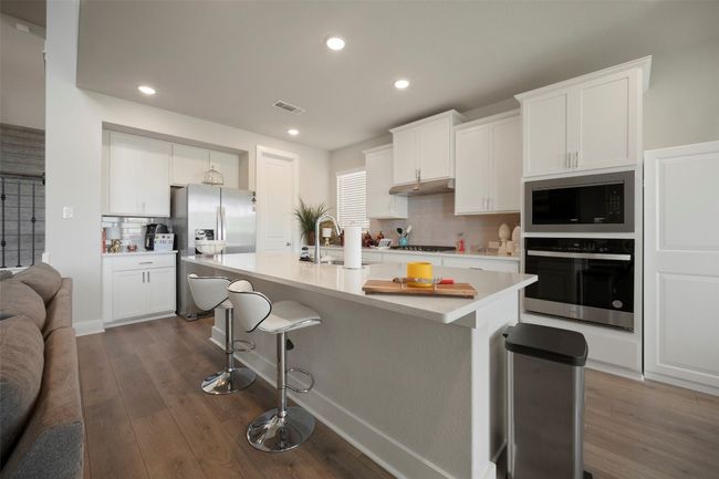Kitchen featuring under cabinet range hood, stainless steel appliances, a breakfast bar area, tasteful backsplash, and dark wood-style floors | Image 18