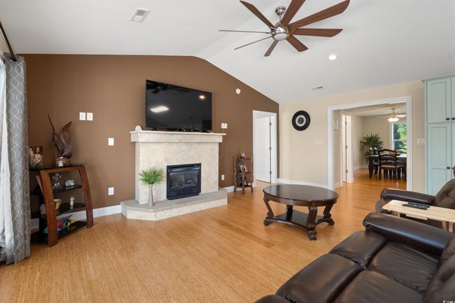 Living area with ceiling fan, light wood-style flooring, vaulted ceiling, a glass covered fireplace, and baseboards | Image 4