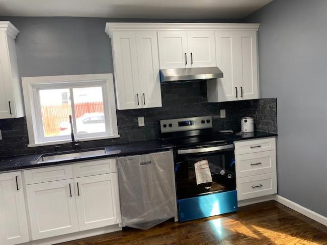 Kitchen with electric range, under cabinet range hood, dishwasher, dark countertops, and backsplash | Image 13