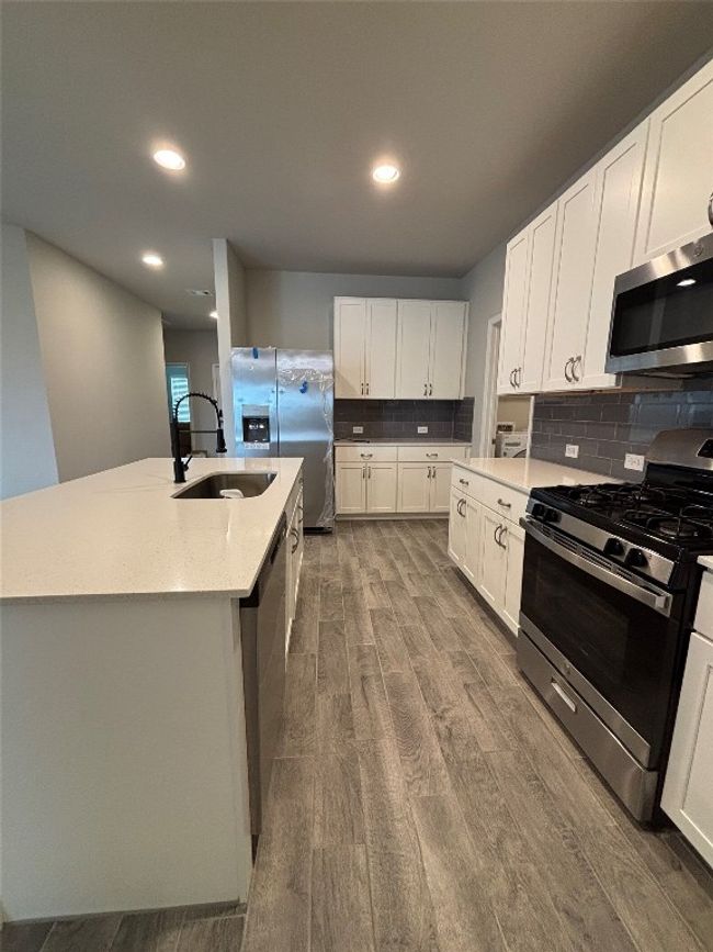 Kitchen with appliances with stainless steel finishes, a sink, dark wood-type flooring, decorative backsplash, and white cabinets | Image 14