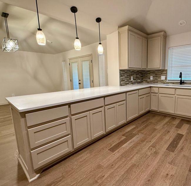 Kitchen featuring lofted ceiling, a peninsula, light wood finished floors, backsplash, and custom cabinetry | Image 7