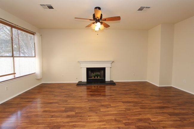 Unfurnished living room with a ceiling fan, wood finished floors, and a fireplace with raised hearth | Image 7