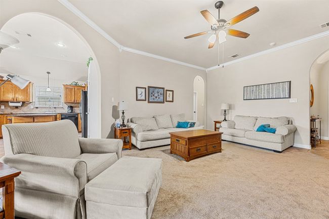 Living area with arched walkways, ornamental molding, ceiling fan, light colored carpet, and baseboards | Image 8
