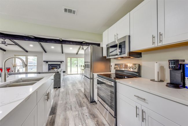 Kitchen featuring appliances with stainless steel finishes, light wood-style floors, white cabinets, beamed ceiling, and light stone countertops | Image 12