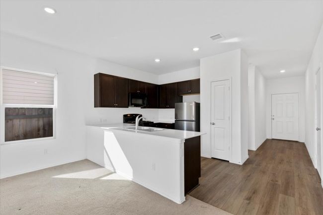 Kitchen with black microwave, freestanding refrigerator, dark brown cabinetry, light countertops, and recessed lighting | Image 4