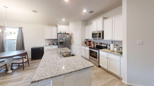 Kitchen with stainless steel appliances, a sink, a chandelier, white cabinetry, and an island with sink | Image 17