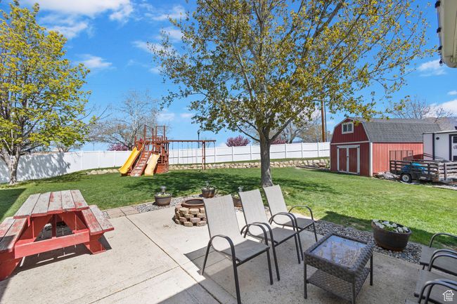 View of patio / terrace featuring a playground, a fenced backyard, an outbuilding, a fire pit, and a storage unit | Image 34
