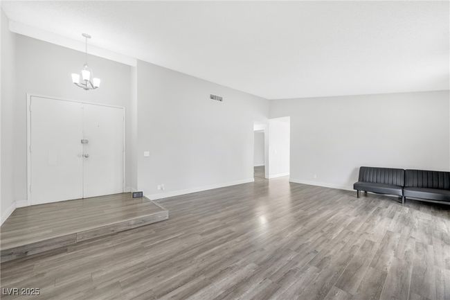 Unfurnished living room featuring visible vents, wood finished floors, a chandelier, and baseboards | Image 9