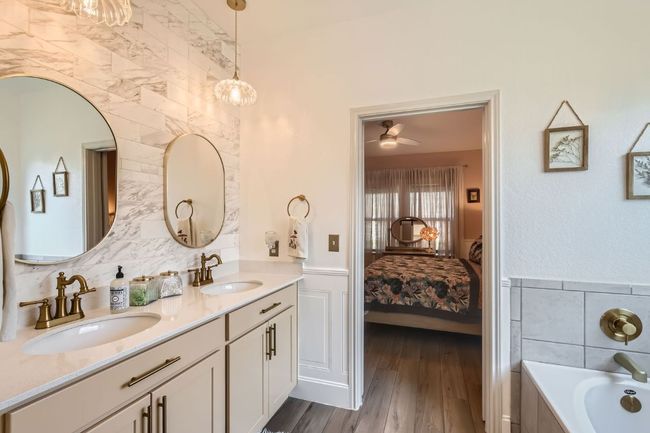 Ensuite bathroom featuring double vanity, a bath, wood finished floors, wainscoting, and a ceiling fan | Image 18