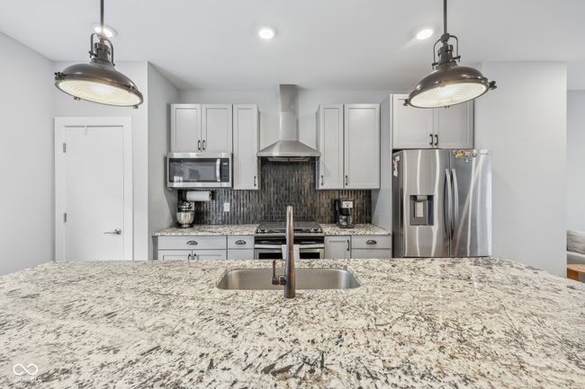 kitchen with wall chimney range hood, light stone countertops, stainless steel appliances, and backsplash | Image 9