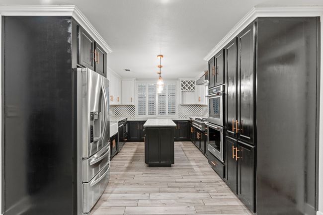 Kitchen with appliances with stainless steel finishes, light wood-style flooring, decorative backsplash, dark cabinets, and a kitchen island | Image 18