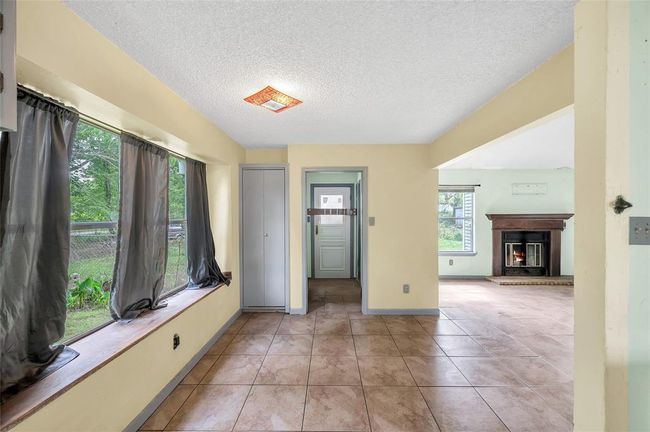 This photo showcases a bright room with large windows and tiled flooring. There's a cozy fireplace visible in an adjacent space, creating a warm and inviting atmosphere. | Image 17