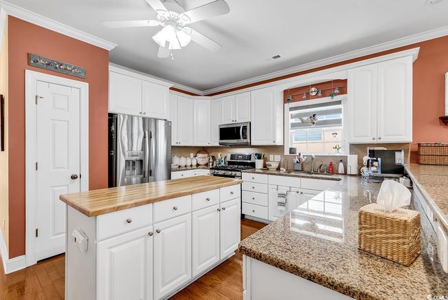 Kitchen featuring white cabinetry, stainless steel appliances, a center island, and hardwood / wood-style floors | Image 12