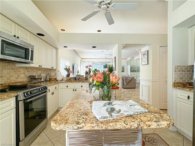 Kitchen with stainless steel appliances, white cabinets, light stone counters, backsplash, and ceiling fan | Image 39