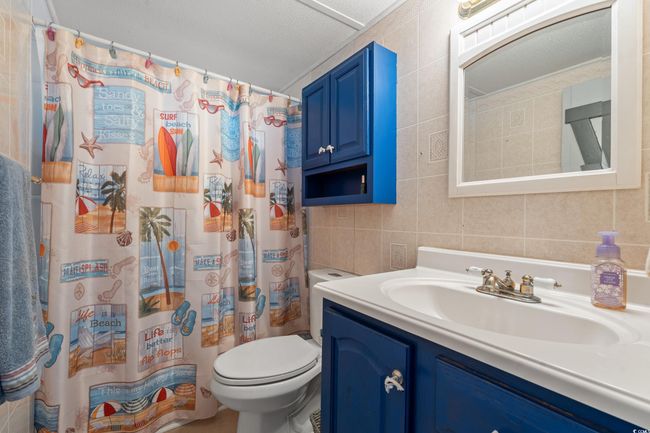 Bathroom with vanity, a shower with shower curtain, tile walls, and toilet | Image 23