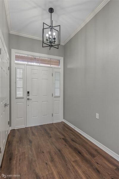 Large entry foyer featuring dark hardwood / wood-style floors, crown molding, and a notable chandelier. There is hall storage in the closet to the right. | Image 3