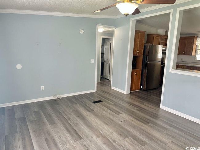 Unfurnished living room featuring ceiling fan, crown molding, wood finished floors, baseboards, and a textured ceiling | Image 13